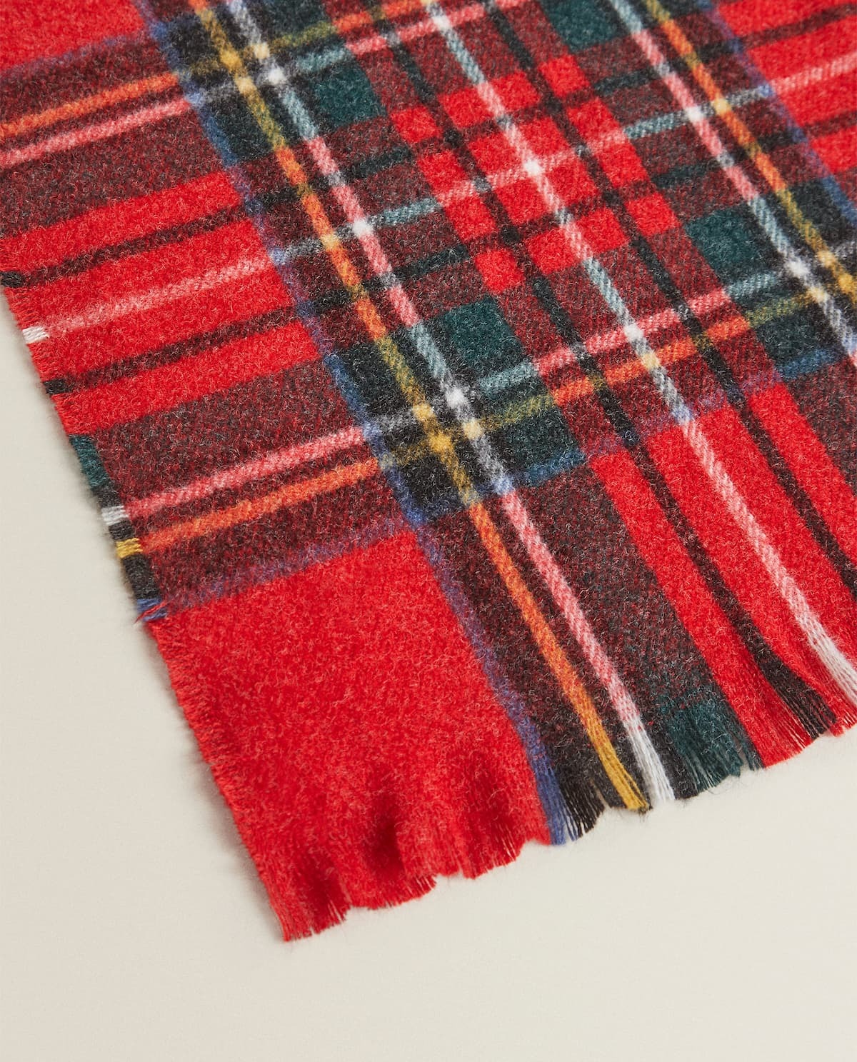 Blanket with a red background and a plaid design.  Fringed edge detail